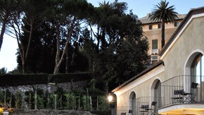 A pool area with lounge chairs and a tent, a building with arched windows and balconies, and a landscaped garden with trees. - Villa Agnese (Sestri Levante)