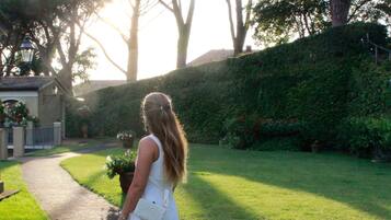 A woman in a white dress walking on a brick pathway in a garden with trees and a lamp post.