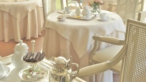 A dining area with two tables set for tea service, each with a teapot, cups, and saucers. The room has a view of a body of water through sheer curtains. - Villa Agnese (Sestri Levante)