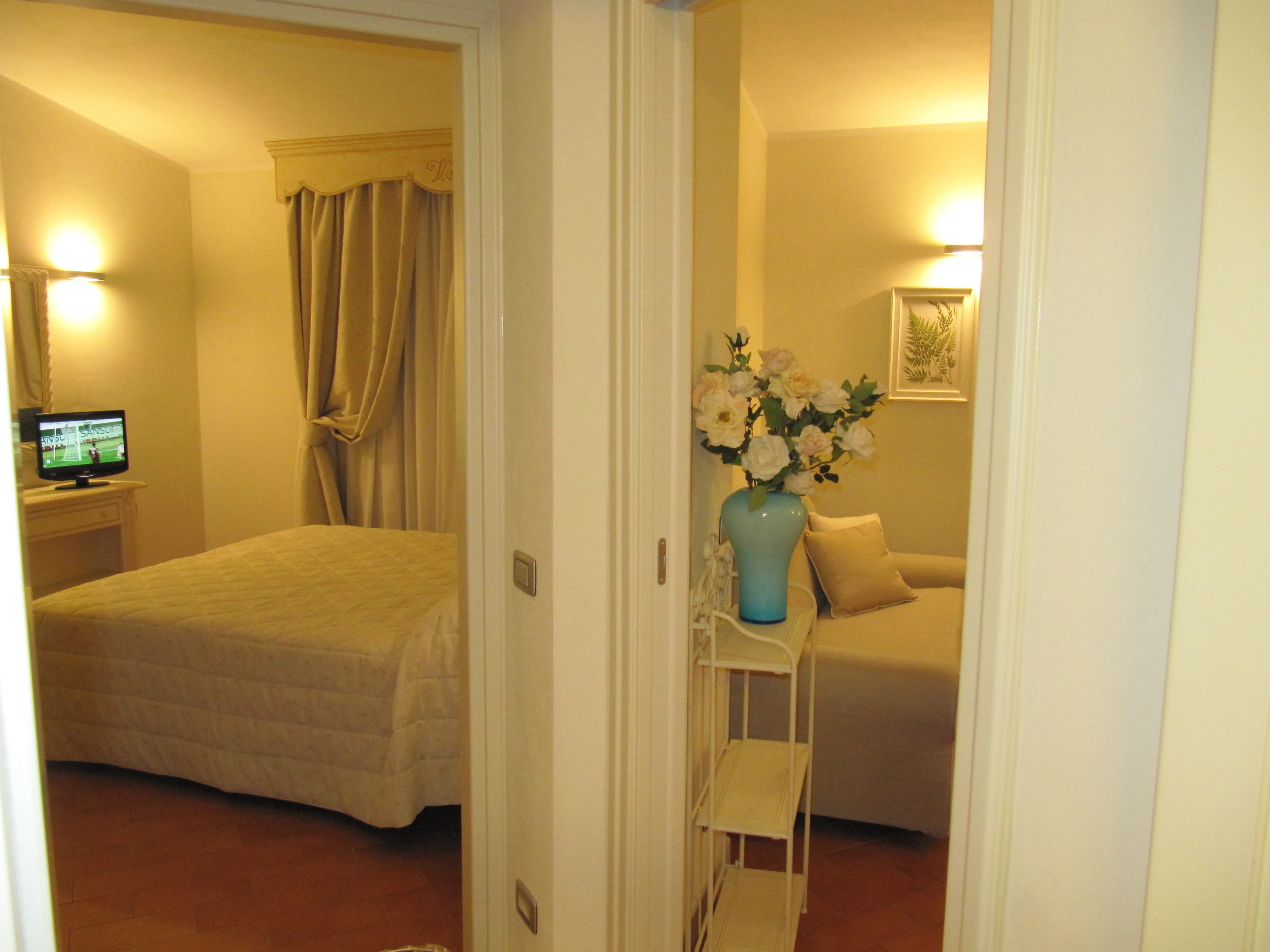 A hotel room with a bed, a TV, a vase with flowers, and a sofa.