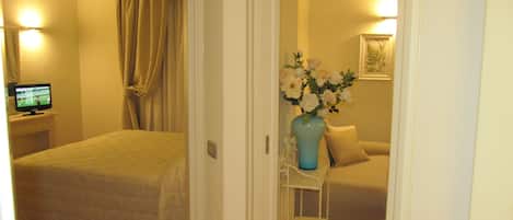 A hotel room with a bed, a TV, a vase with flowers, and a sofa.