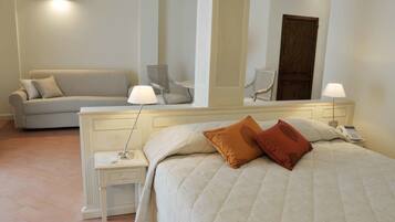 Quarto de hotel com cama, mesa de cabeceira, luminária, cadeira e sofá.