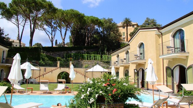A poolside area with lounge chairs, umbrellas, and a staircase leading to a building with balconies. - Villa Agnese (Sestri Levante)