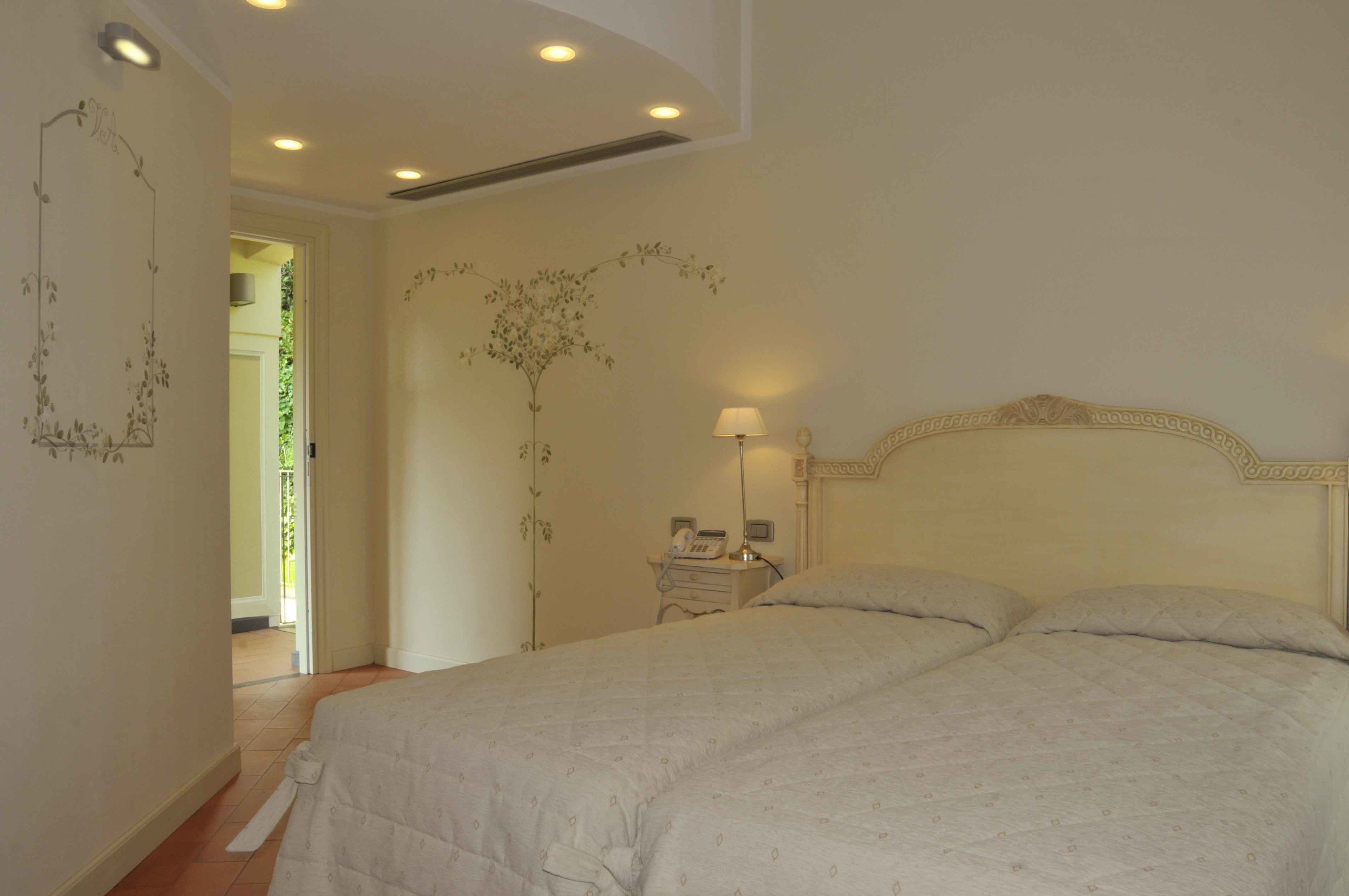 Un dormitorio con una cama grande, una mesita de noche con lámpara y una pared decorada con motivos florales.