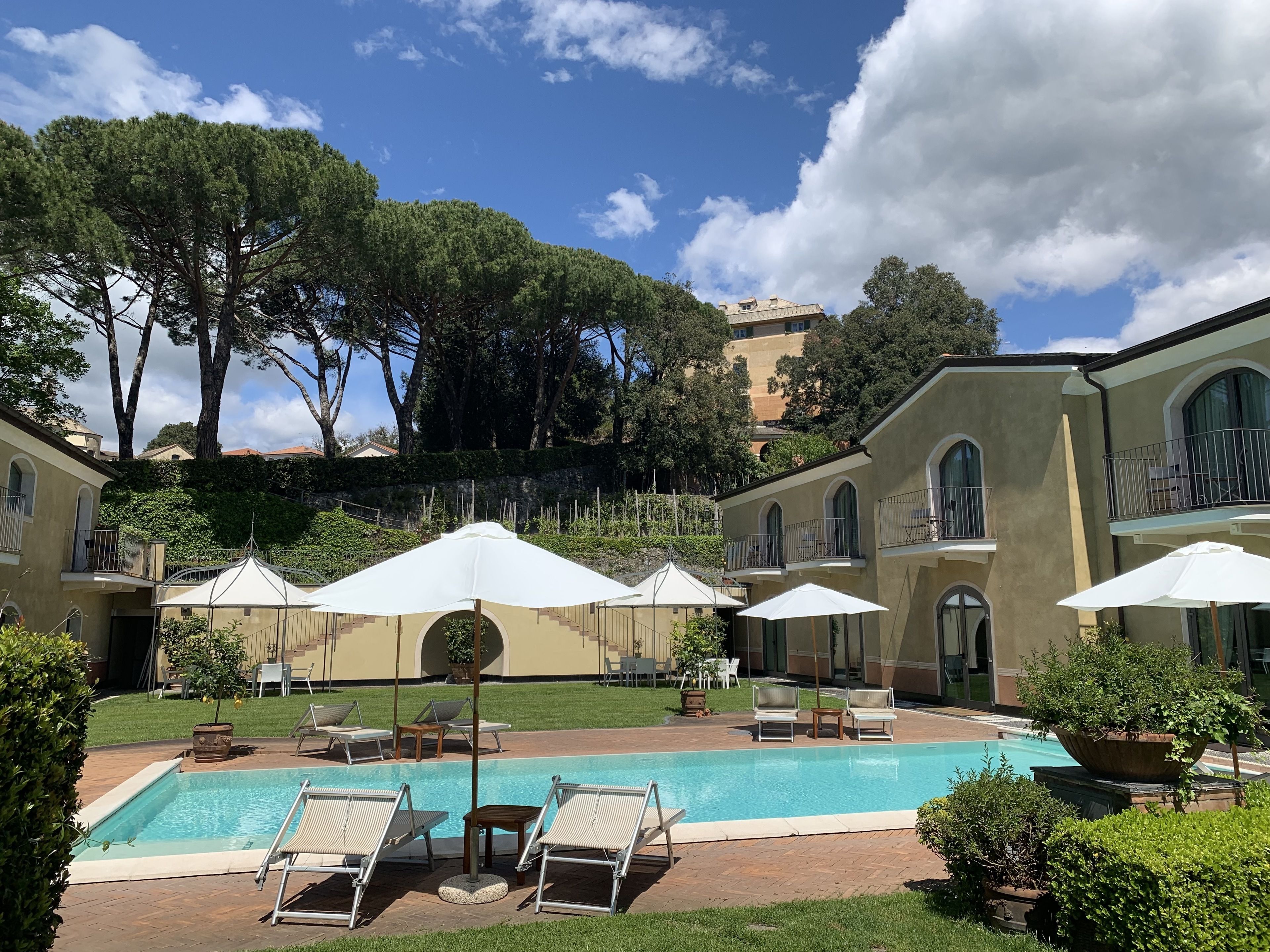 A pool area with lounge chairs and umbrellas, surrounded by a building with arched windows and balconies.