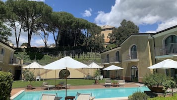 A pool area with lounge chairs and umbrellas, surrounded by a building with arched windows and balconies.