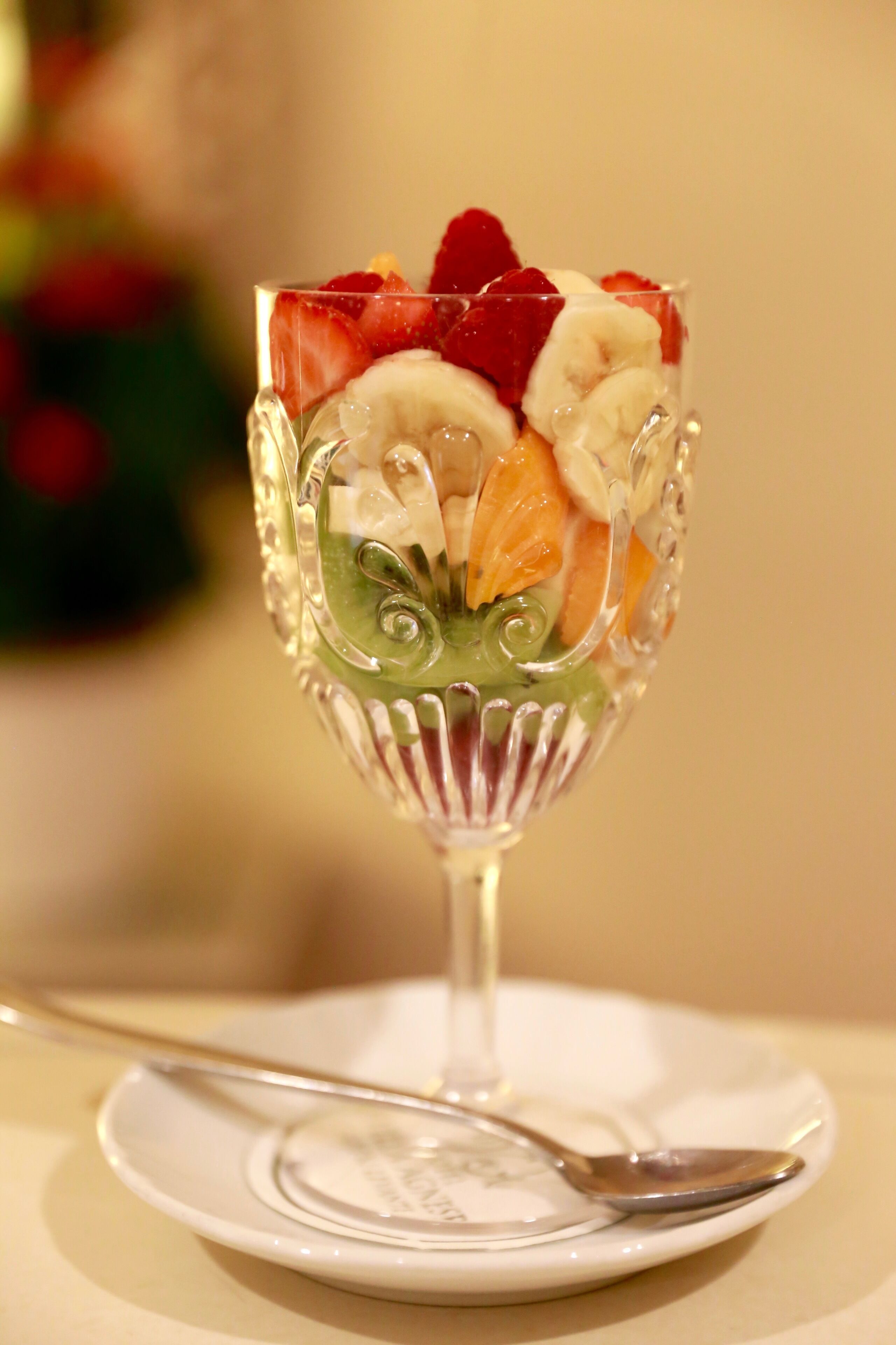 Un dessert in un bicchiere su un piatto bianco con un cucchiaio.