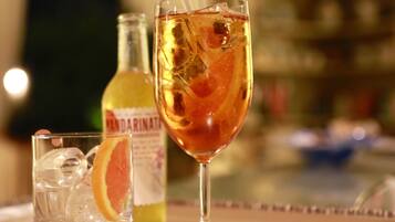 A bar setting with a glass of amber-colored drink, ice cubes, and a slice of orange. A bottle labeled "MANDARIN" is visible in the background.