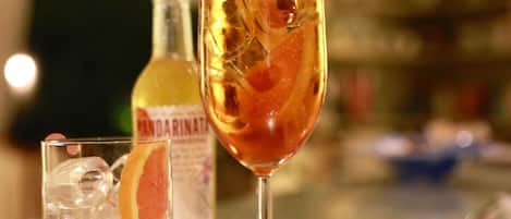 A bar setting with a glass of amber-colored drink, ice cubes, and a slice of orange. A bottle labeled "MANDARIN" is visible in the background.