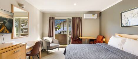 A hotel room with a bed, a desk, a chair, a dresser, a window with curtains, and a painting on the wall.