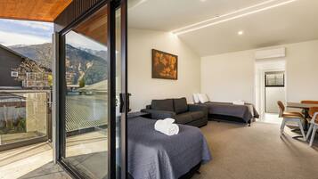Quarto de hotel moderno com varanda, sofá, cama e área de jantar.