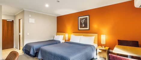A hotel room with two beds, a desk, a chair, and a framed picture on the wall.