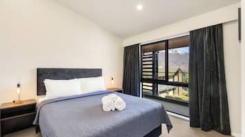 A hotel room with a bed, a nightstand, a lamp, a window with curtains, and a view of mountains.