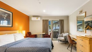 A hotel room with a bed, desk, chair, and a view of the outdoors. - Queenstown Motel Apartments (Queenstown)