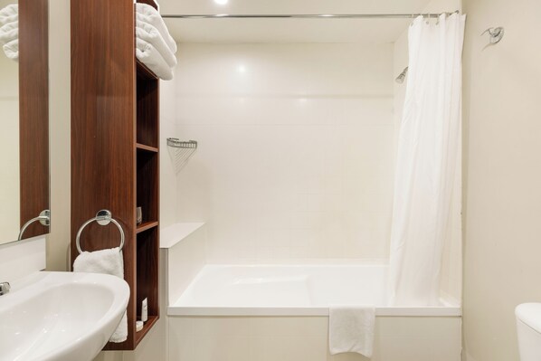 Un baño con lavamanos, espejo, estante de madera y bañera con cortina de ducha.