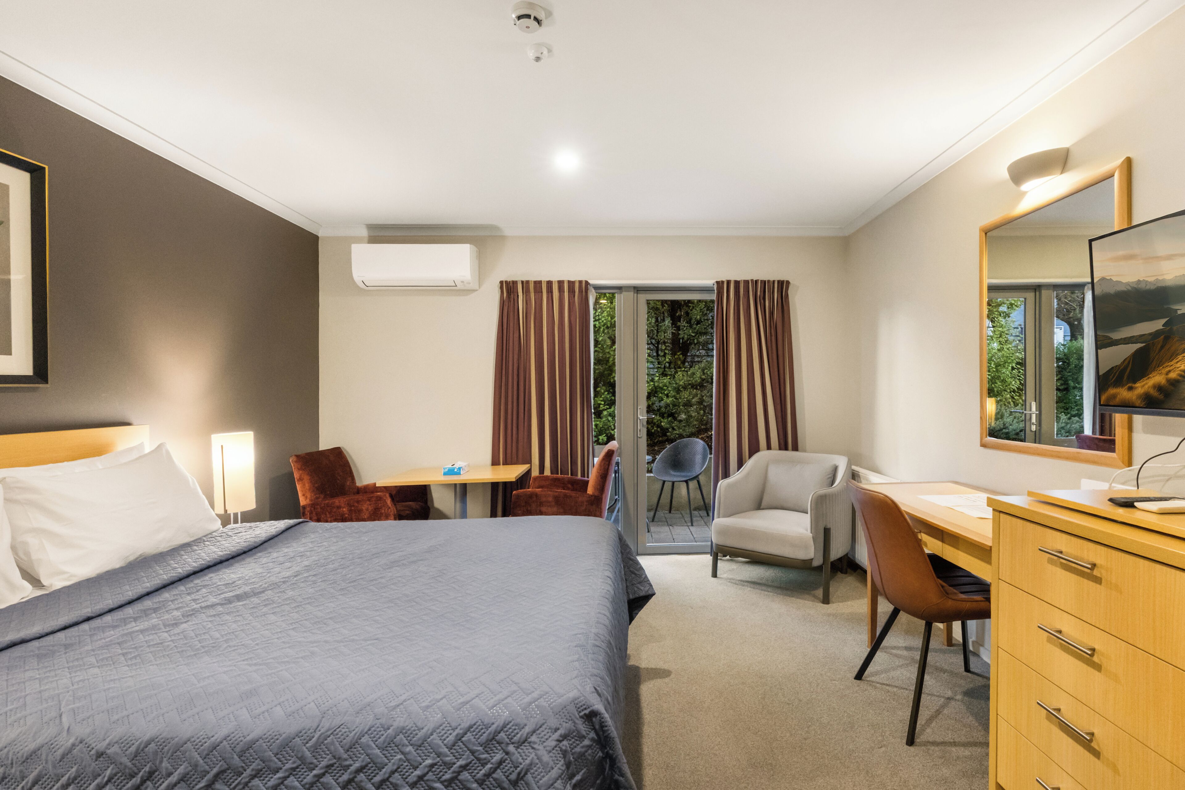 A hotel room with a bed, a desk, a chair, a TV, and a window with curtains.