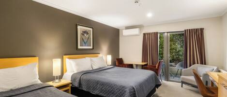 Une chambre d’hôtel avec deux lits, un bureau, une chaise, une table, un appareil de climatisation et une fenêtre avec des rideaux.