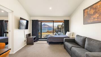 A modern hotel room with a bed, a sofa, a TV, and a large window offering a mountain view.