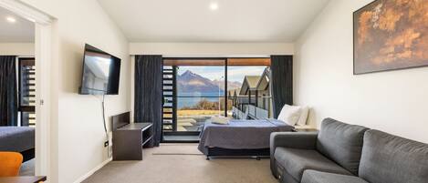 Habitación de hotel moderna con cama, sofá, televisor y ventana grande con vistas a la montaña.