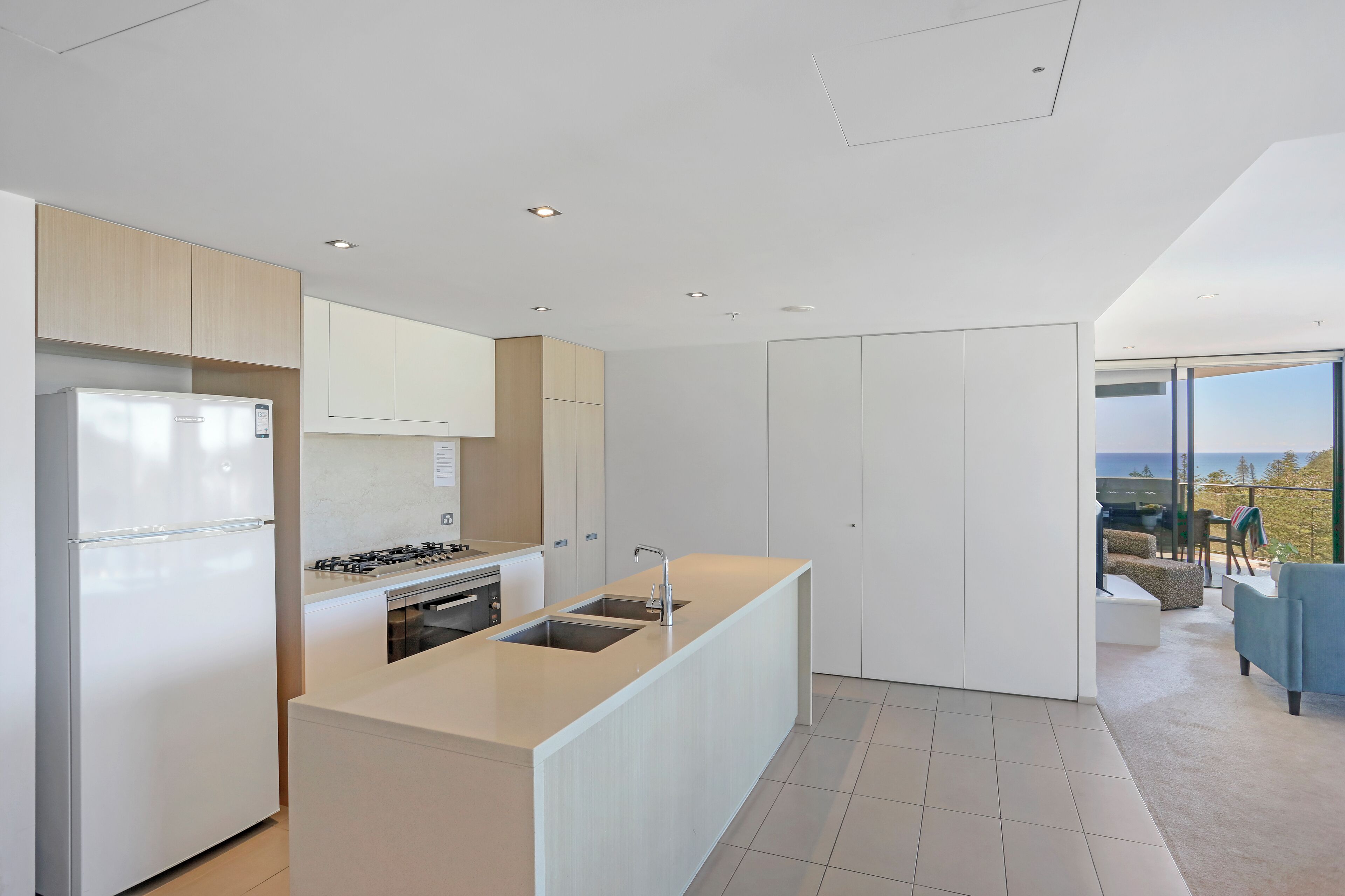 Une cuisine moderne dotée d’un îlot central, d’appareils électroménagers intégrés et donnant sur un balcon extérieur.