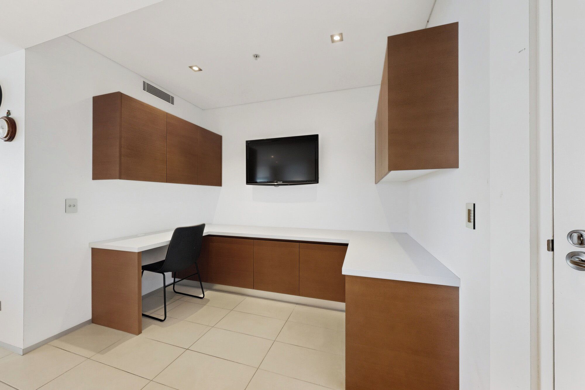 A modern room with a white desk, a black chair, a mounted TV, and built-in wooden storage units.