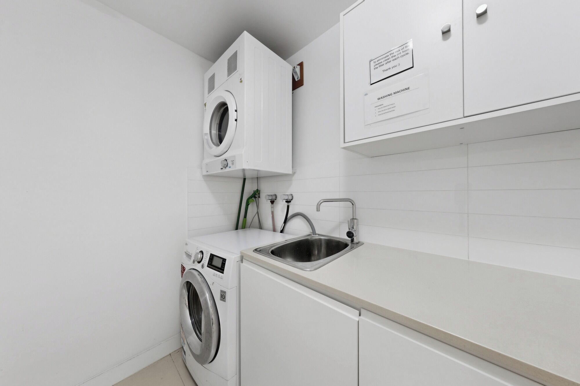A laundry room with a washing machine, a sink, and cabinets.