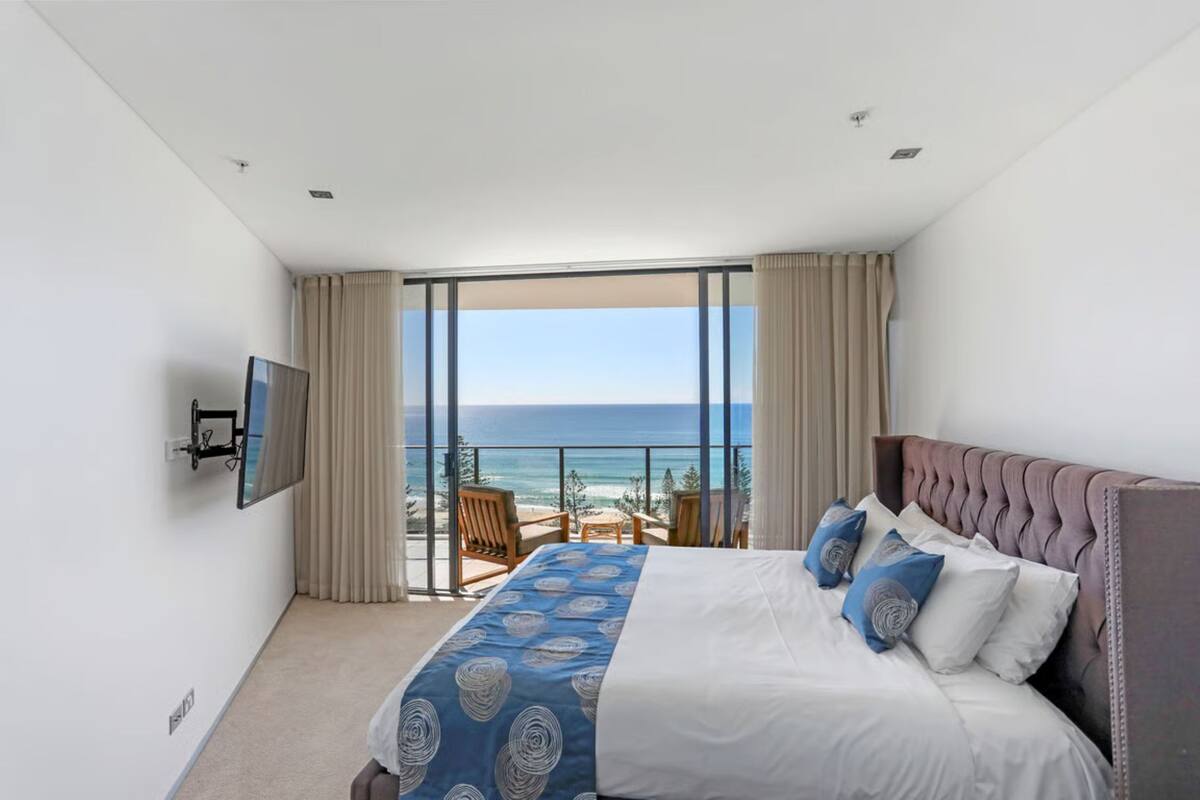 Quarto com cama, televisão, varanda com vista para o mar e uma cadeira.