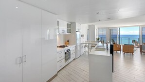 A modern kitchen with white cabinetry, a central island, and a view of the ocean. - Ambience on Burleigh Beach (Burleigh Heads)