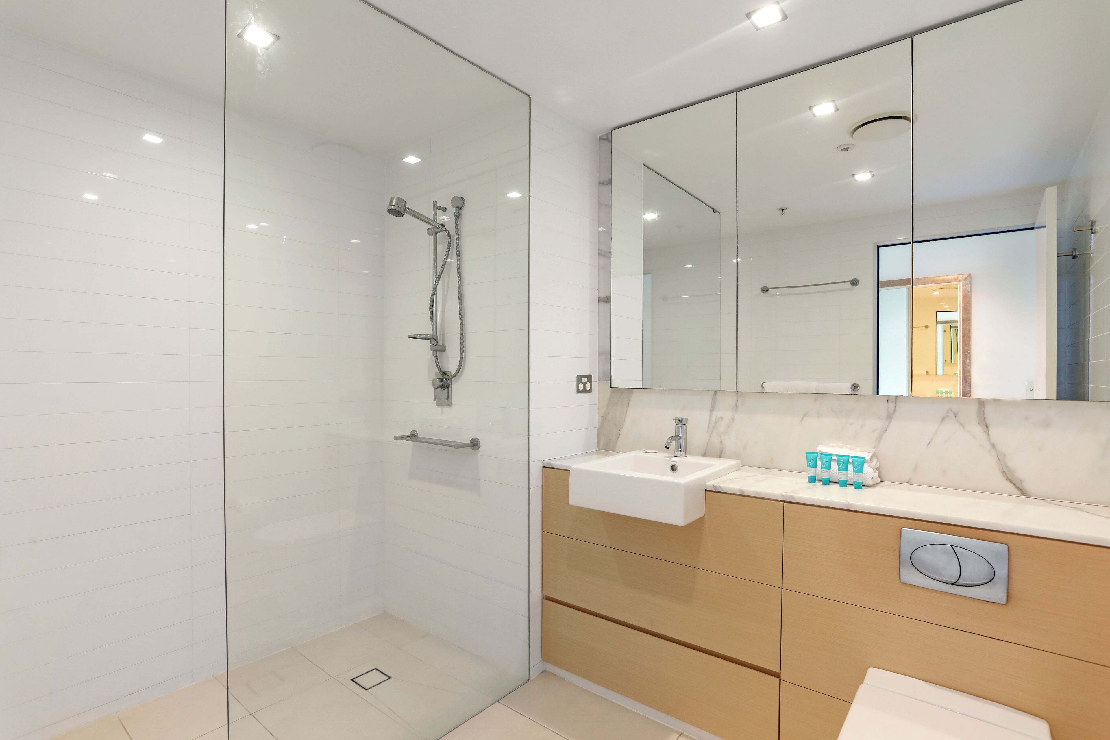 Un baño moderno con ducha de vidrio, tocador con lavamanos y un espejo grande.