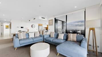A modern living room with a sectional sofa, a round coffee table, and a view of the city through large windows.
