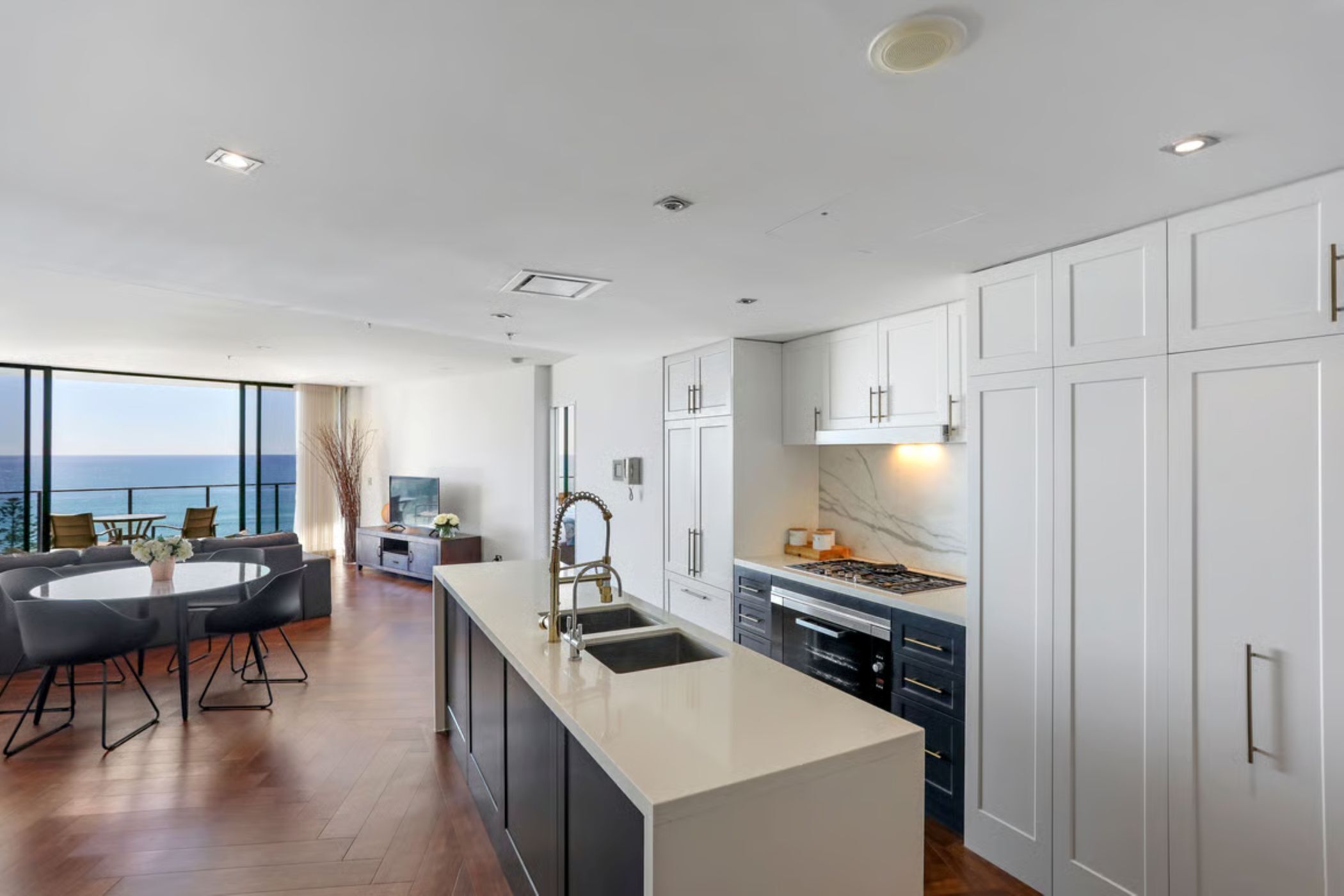 A modern kitchen with a large island, white cabinetry, and a view of the ocean.