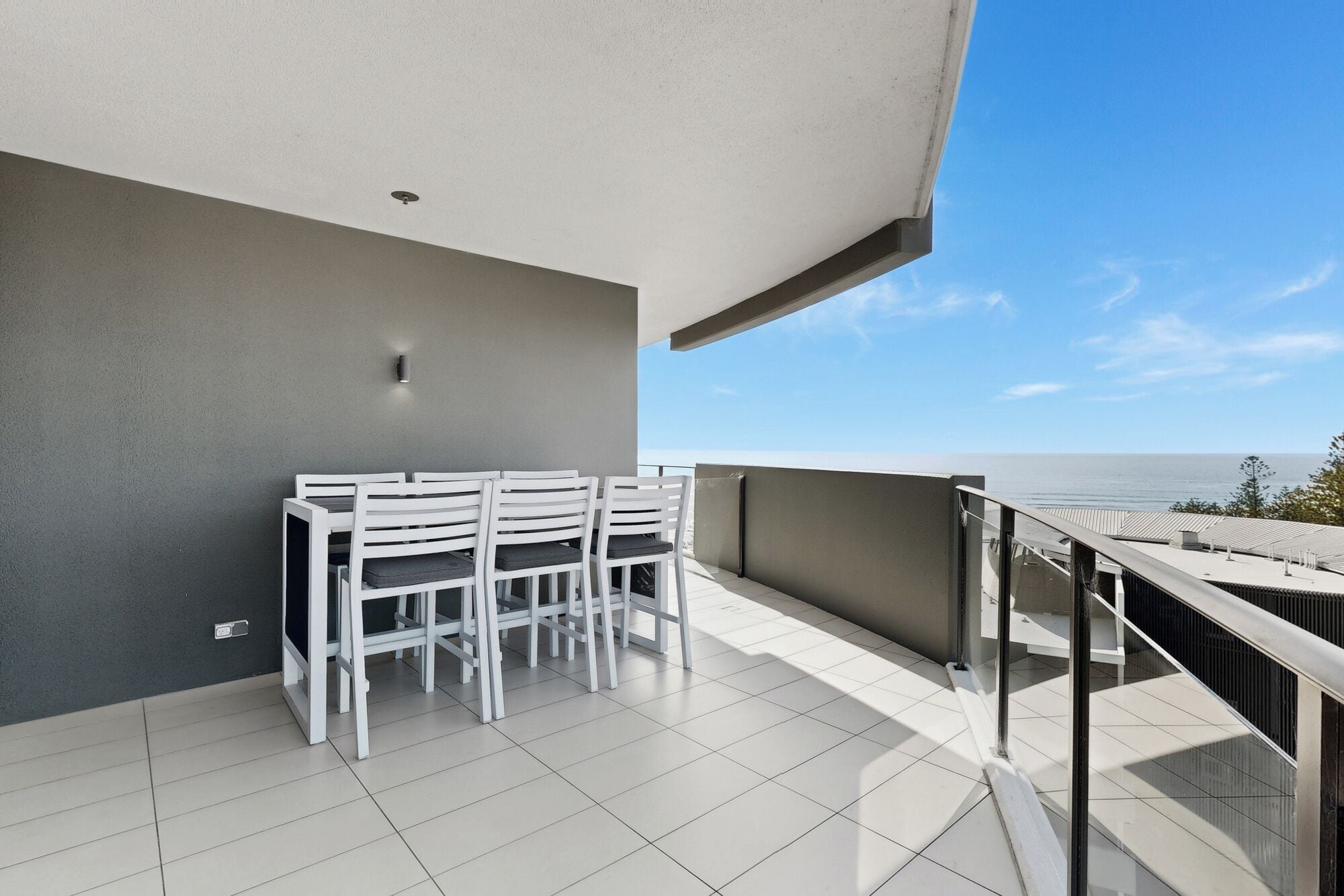 Un balcon avec une table et des chaises, une vue sur la mer et un ciel dégagé.