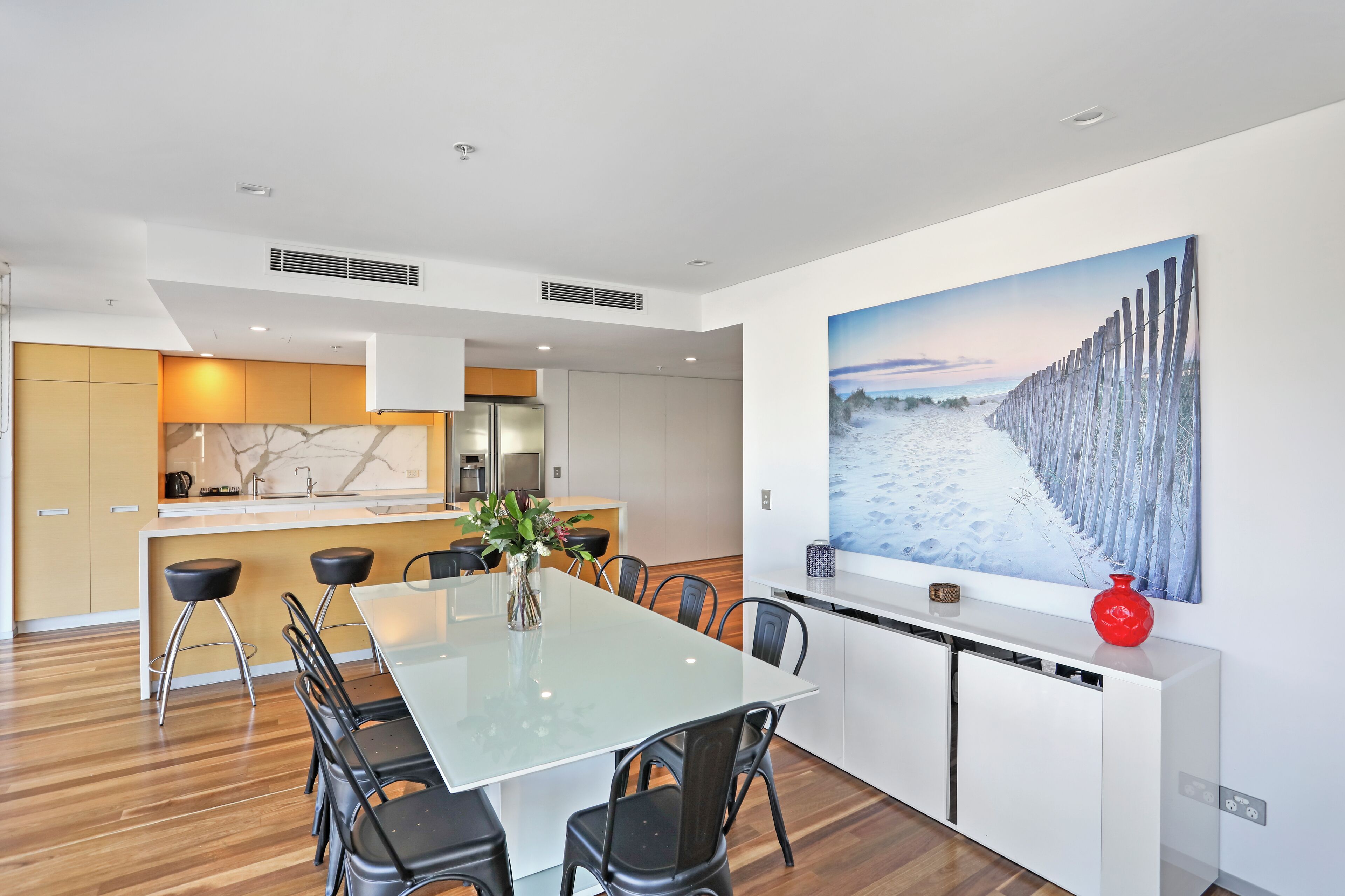 Una cocina moderna con una isla central, armarios blancos y un cuadro grande que muestra una playa nevada.