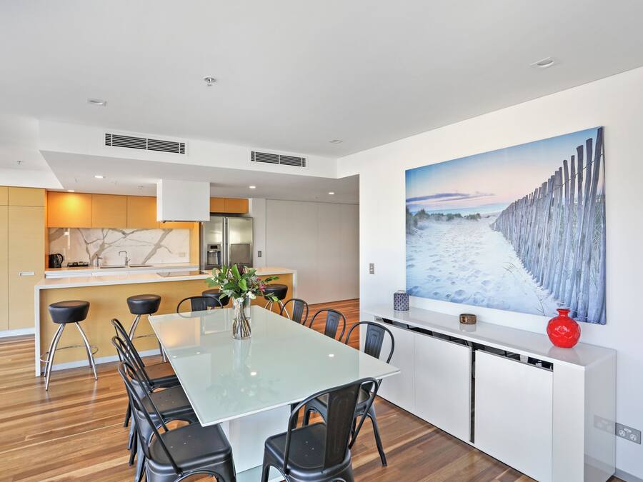 Una cocina moderna con una isla central, armarios blancos y un cuadro grande que muestra una playa nevada.