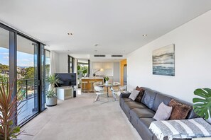 A modern living area with a sofa, TV, dining table, and kitchen in the background.