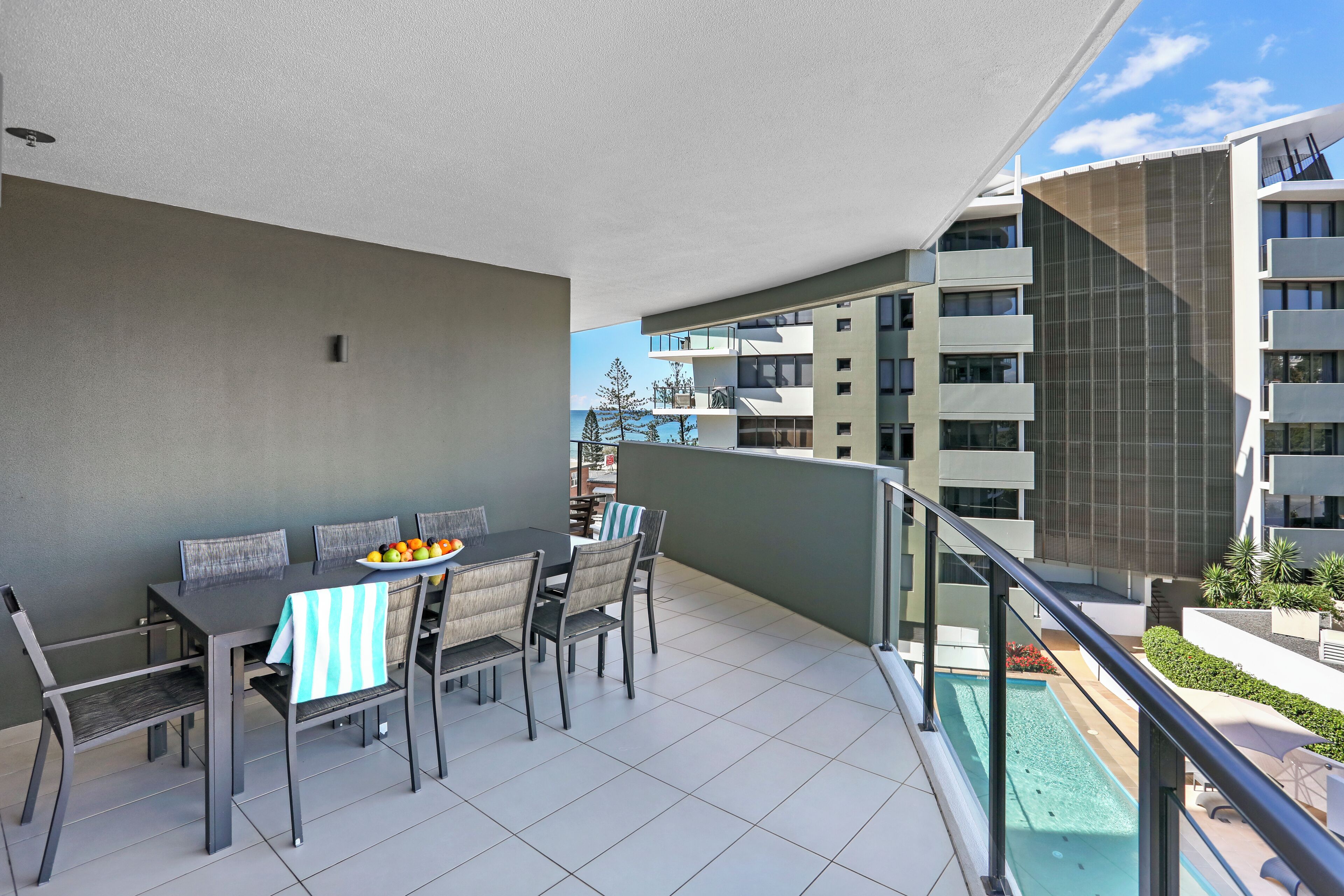 A balcony with a dining table set for four, overlooking a residential area and a body of water.