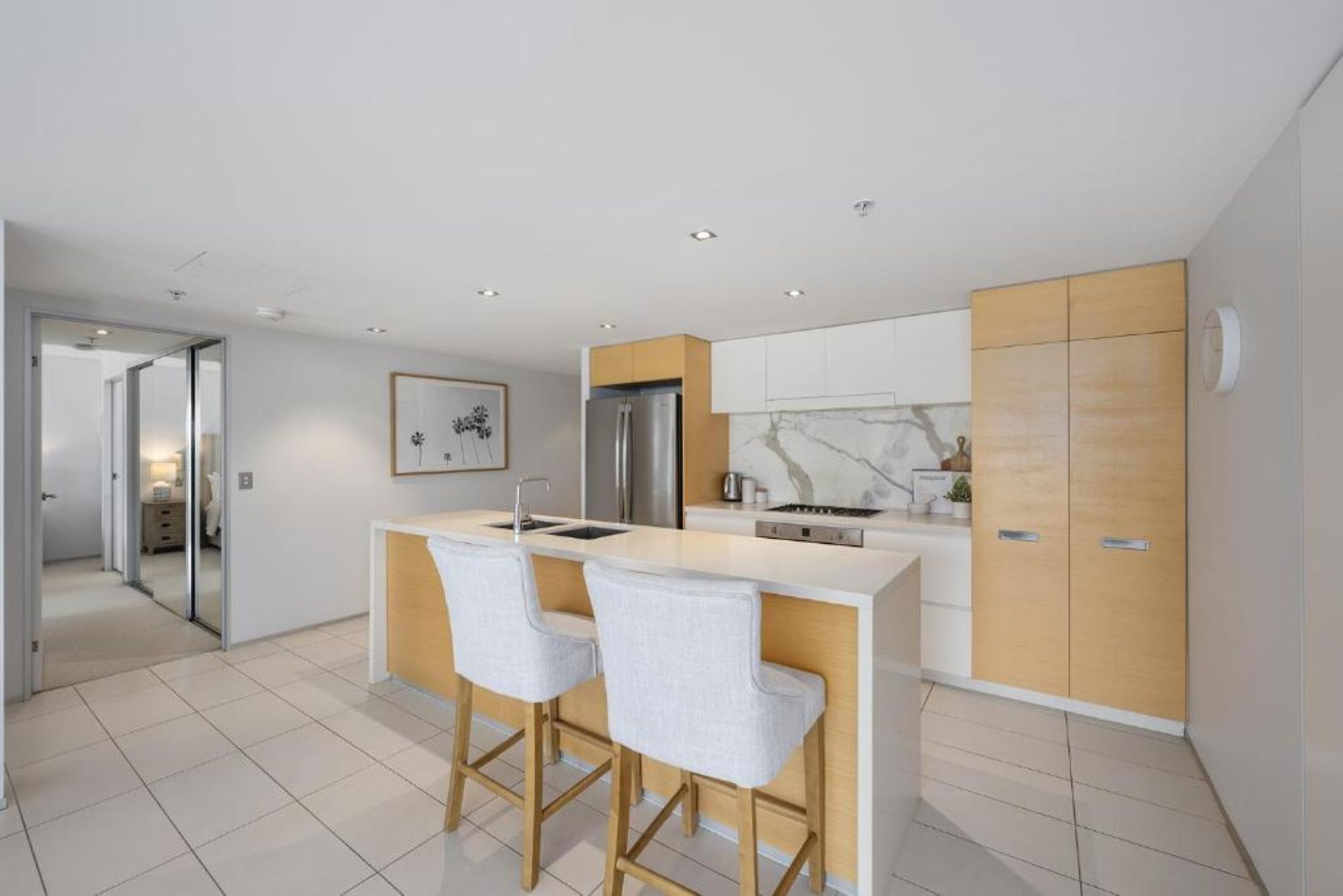 Een moderne keuken met een centraal eiland, twee barkrukken, een koelkast en een marmeren spatwand.