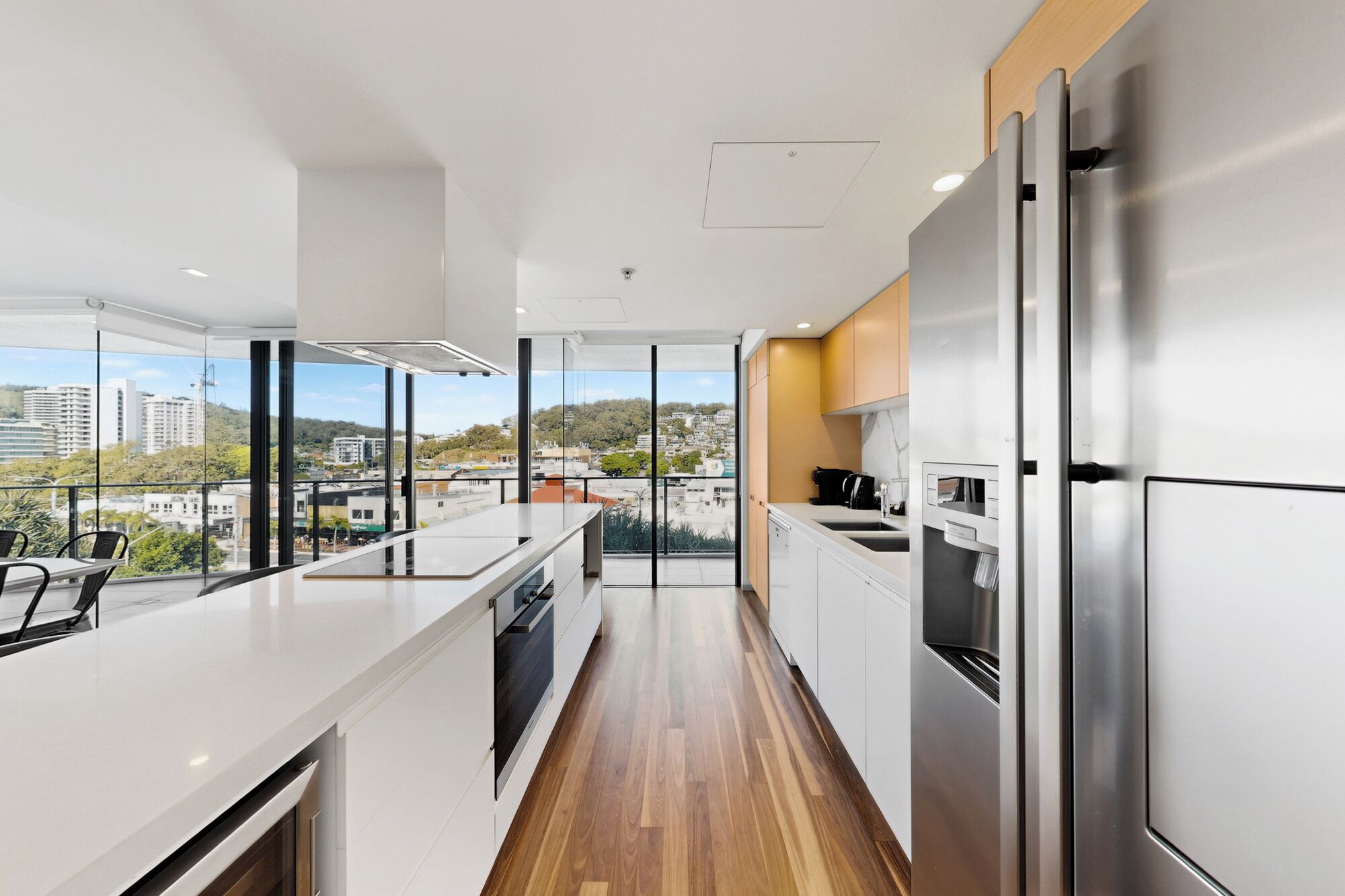 A modern kitchen with a stainless steel refrigerator, a built-in oven, and a large window offering a city view.