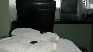 Hotellihuone, jossa on sänky, tuoli, kirjoituspöytä, jossa on televisio, ja ikkuna.