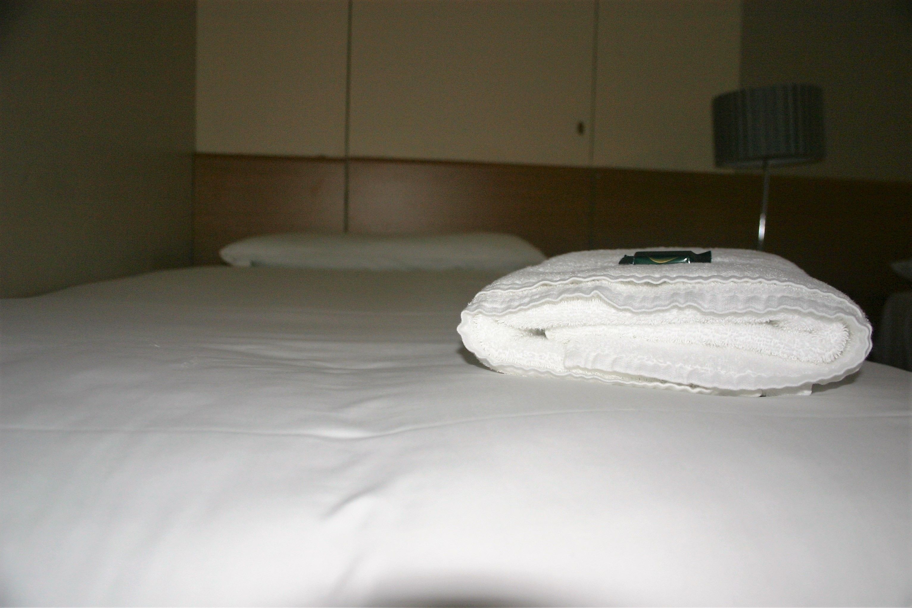 A hotel room with a neatly made bed, a pillow, and a lamp on a bedside table.