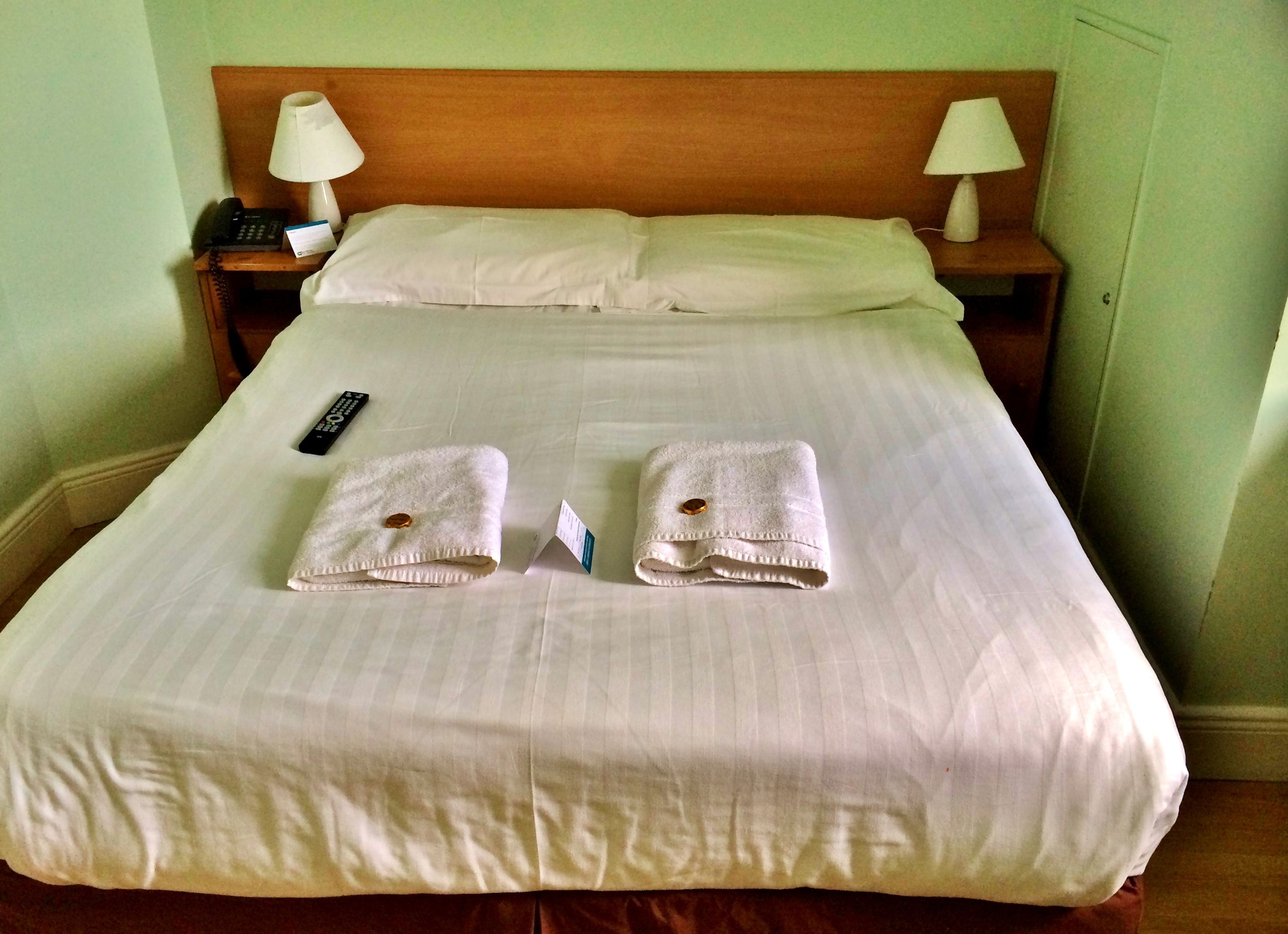 A neatly made bed with two folded towels and a remote control on the bed.