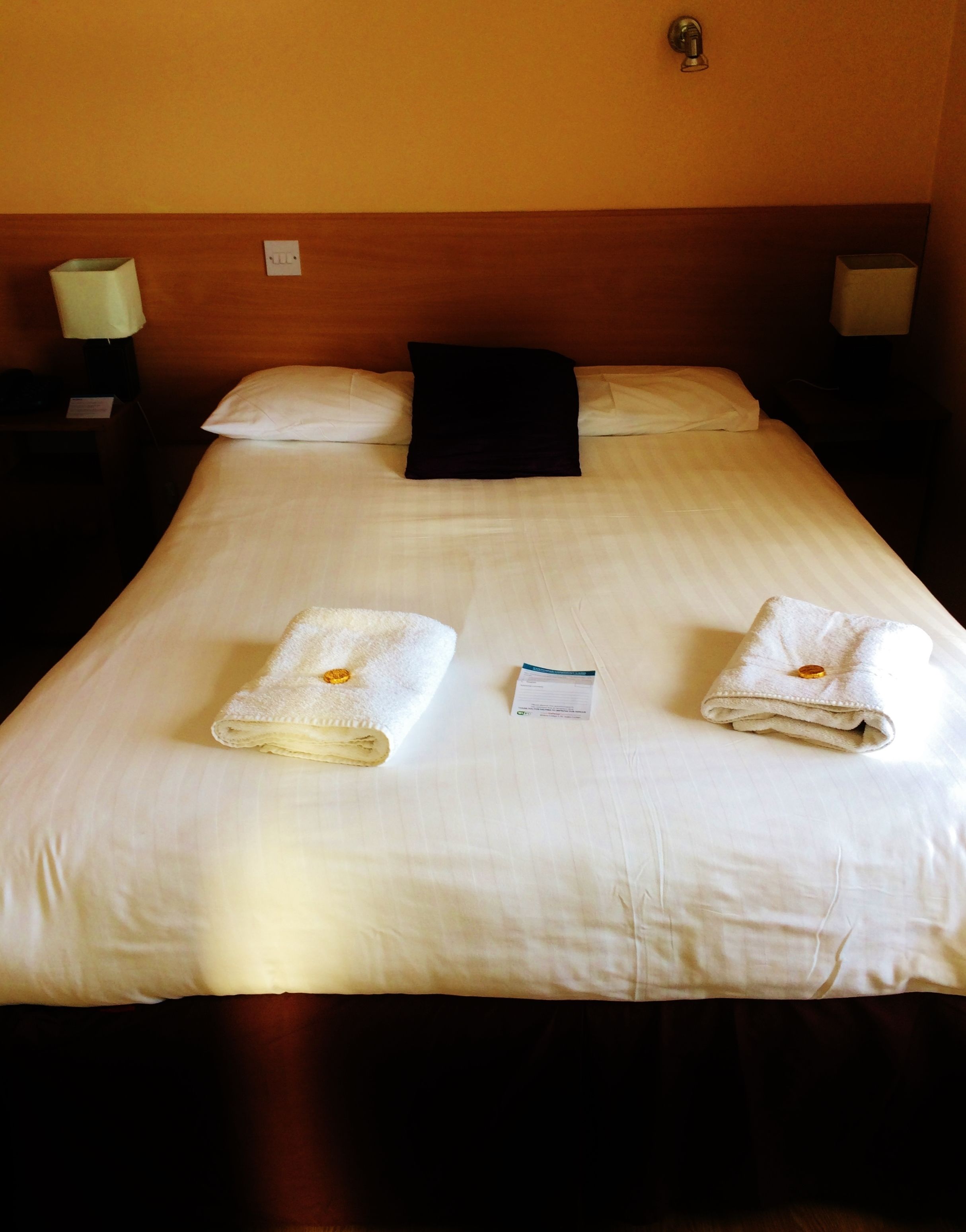 Una cama bien hecha con dos toallas dobladas y una tarjeta sobre la cama.