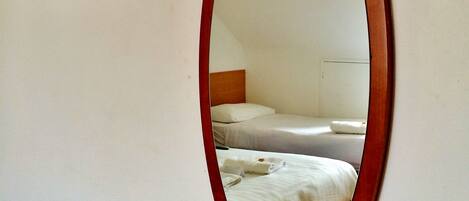 A room with a bed, a wooden-framed mirror, and a framed picture on the wall.