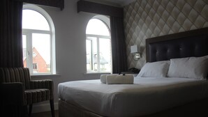 A hotel room with a large bed, a chair, and two windows with curtains. - St Judes Lodge (Galway)