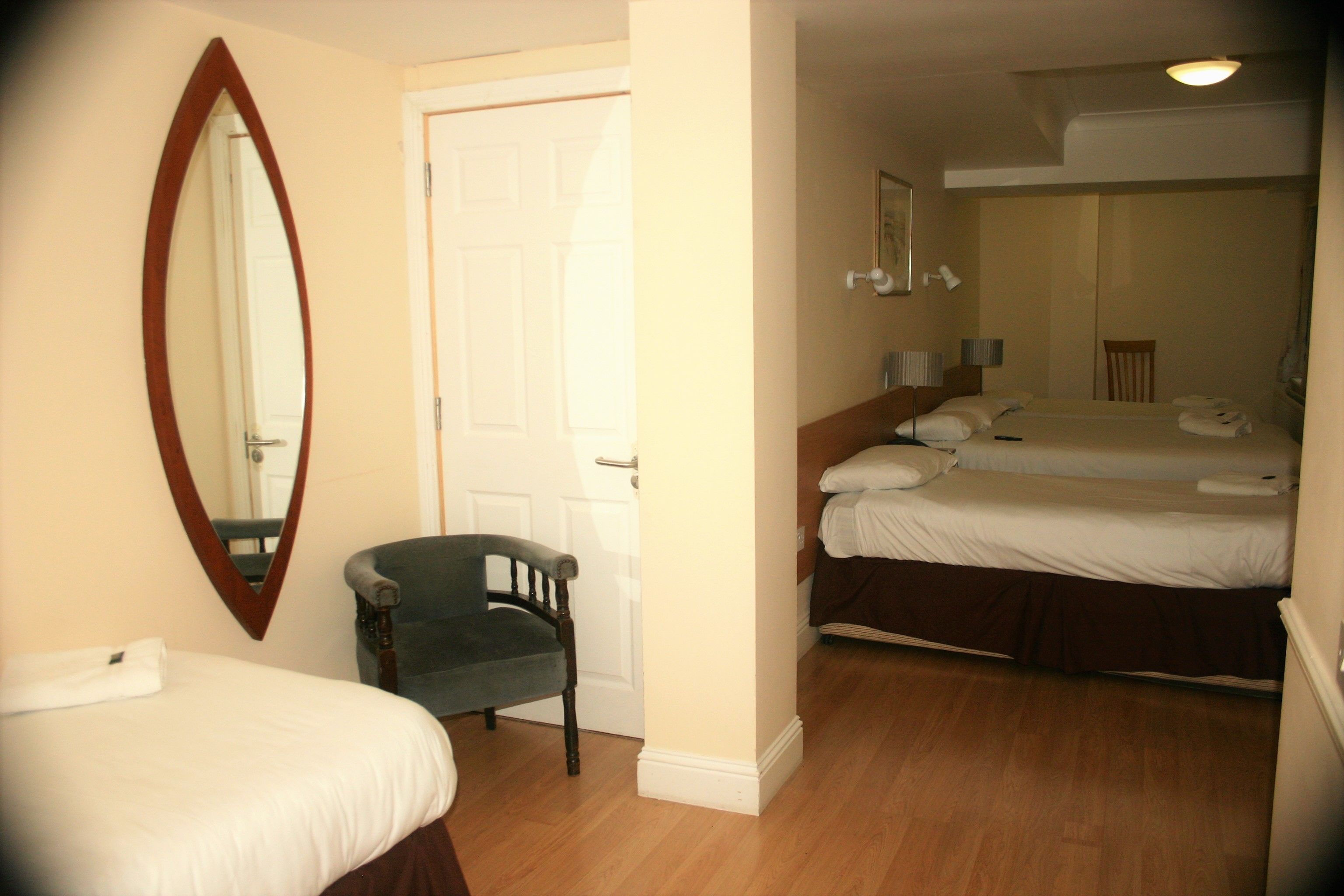 A hotel room with two single beds, a chair, a large mirror, and a door.