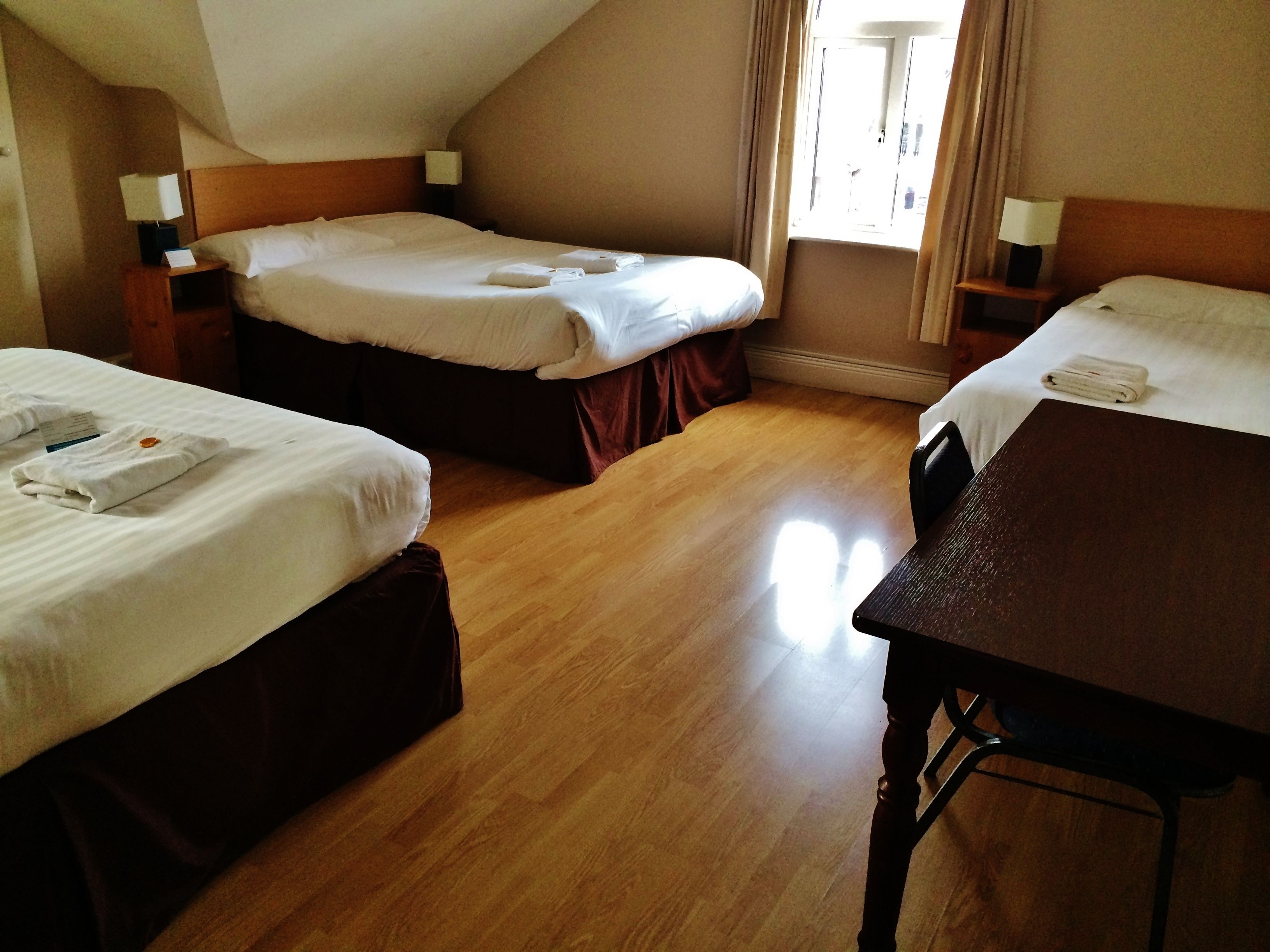 A hotel room with two beds, wooden flooring, and a table.