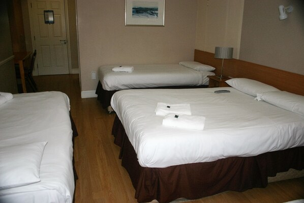 A hotel room with two single beds, each with white linens and towels, a wooden floor, a door, and a framed picture on the wall. - St Judes Lodge (Galway)