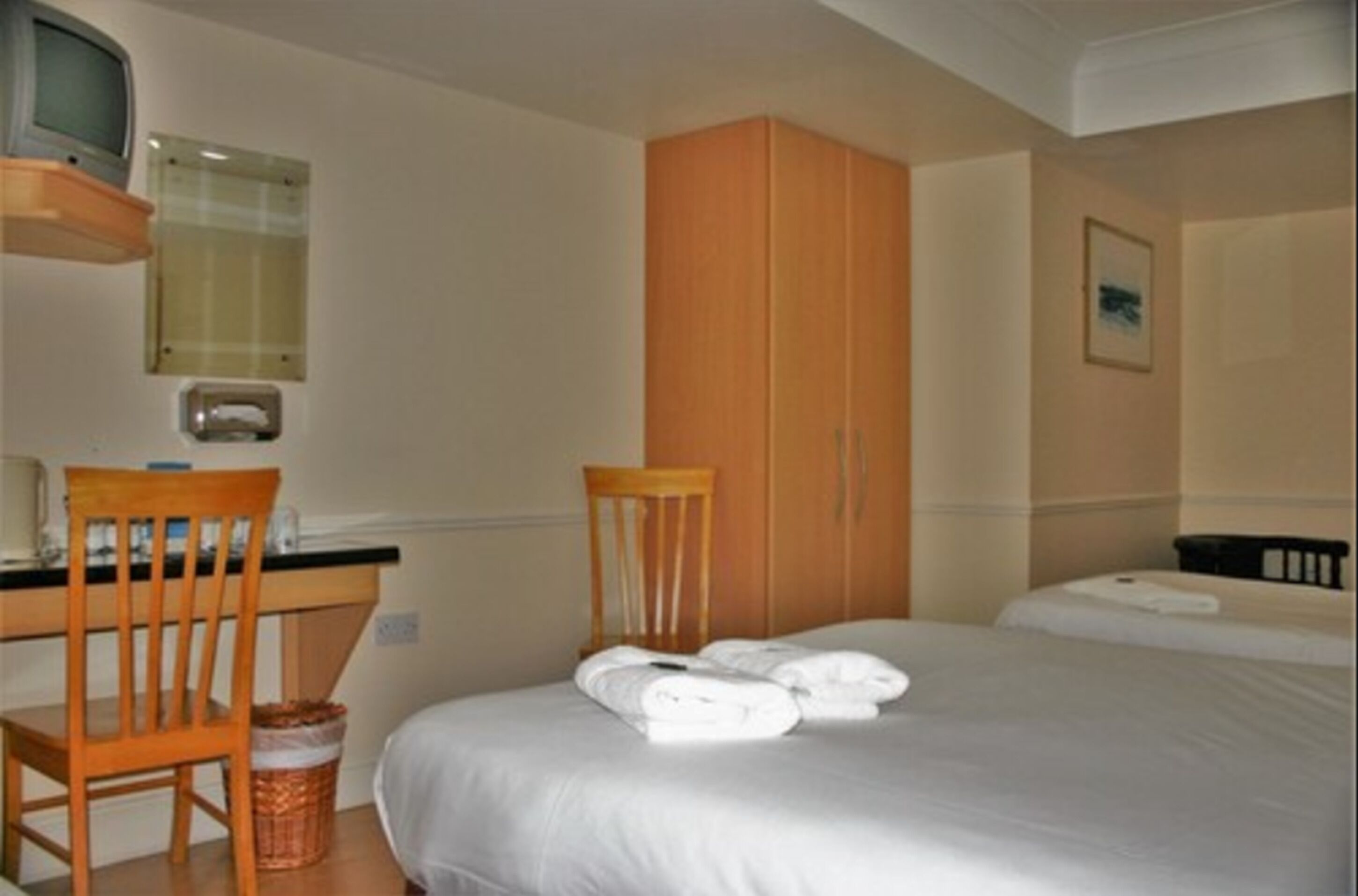 Una habitación de hotel con una cama, una silla de madera, un escritorio, un televisor y un armario.