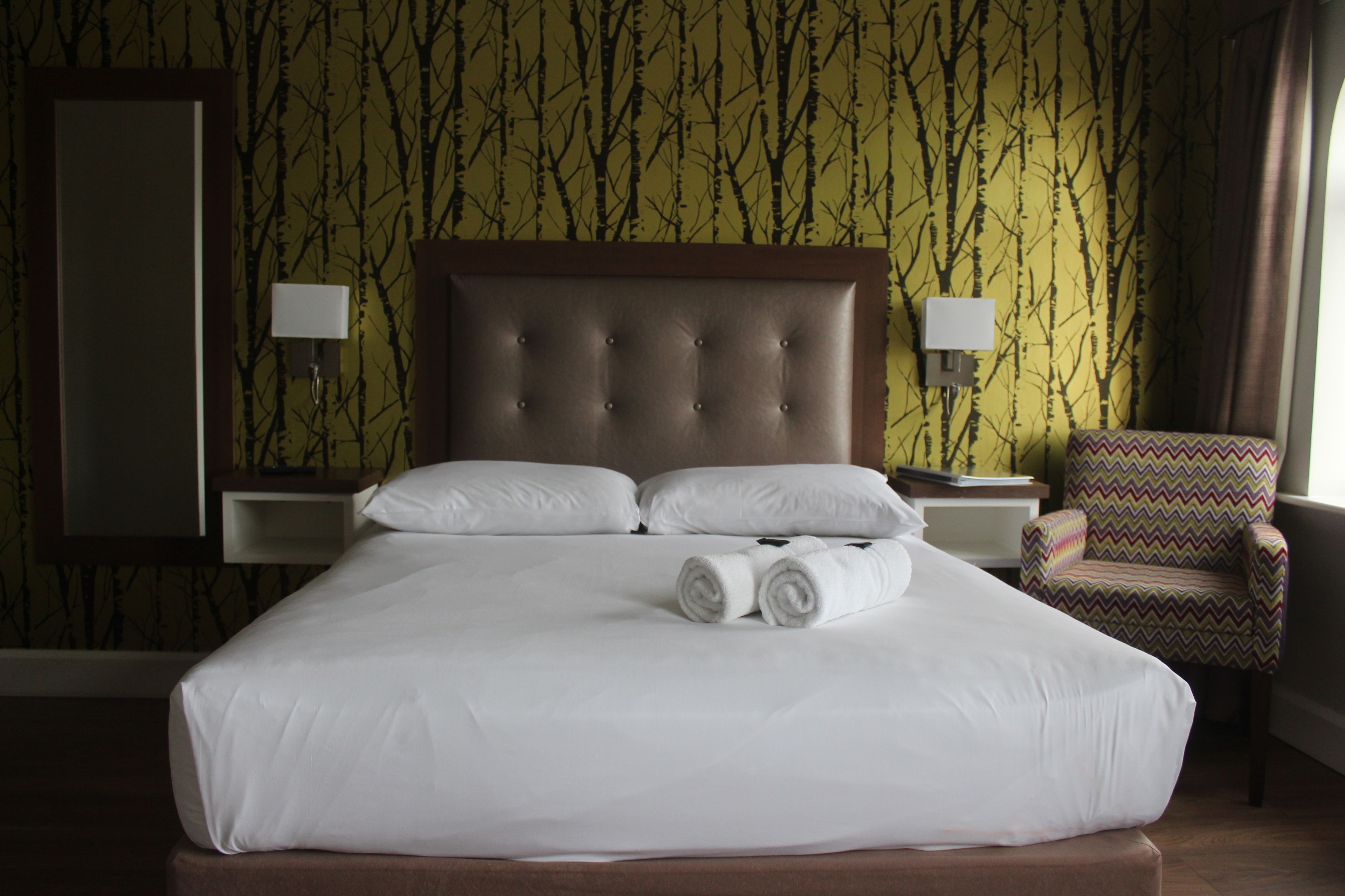 A hotel room with a large bed, two bedside lamps, a chair, and a mirror on the wall.