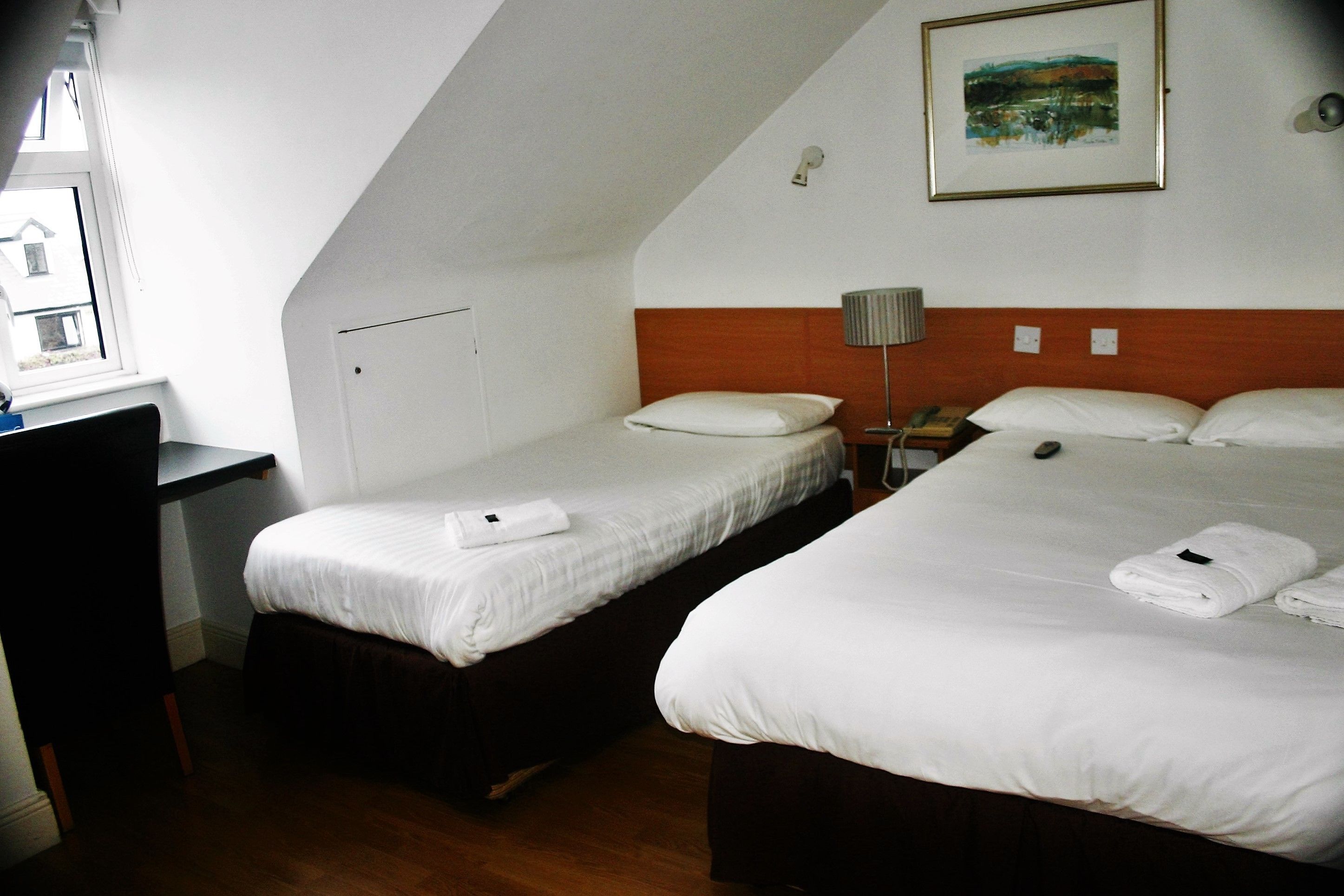 A hotel room with two beds, a desk, and a window.